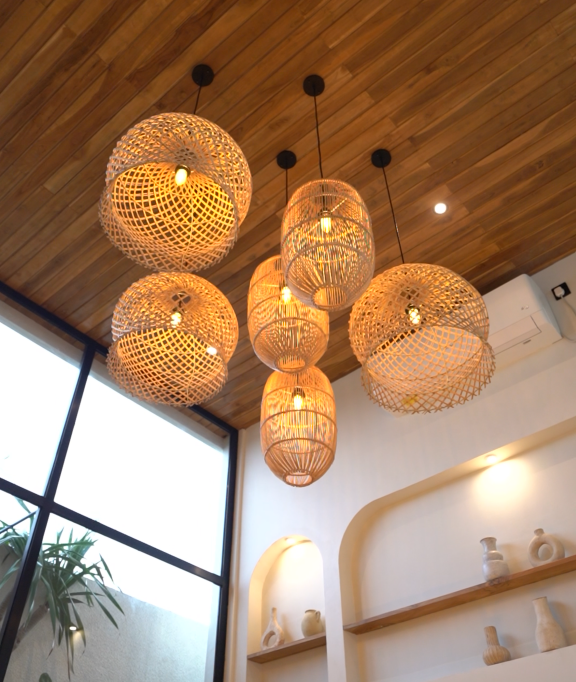 Multiple wicker aesthetic pendant light fixtures hanging from a wooden ceiling in a modern interior with large window