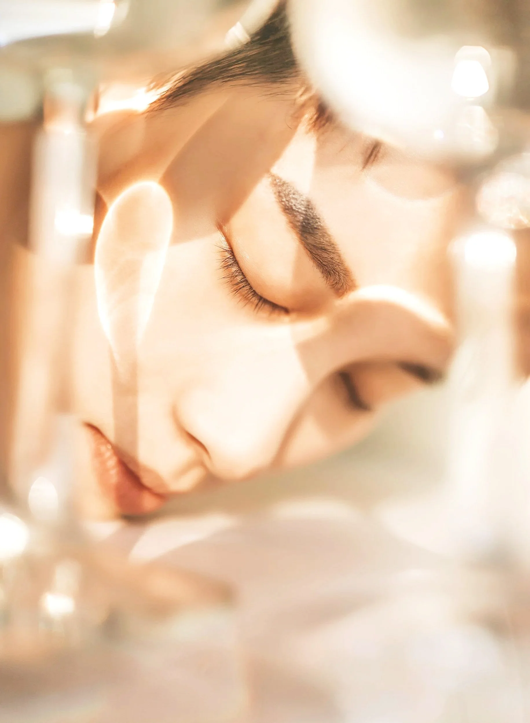 Close-up of a person's face with closed eyes, appearing to be resting or sleeping, with soft lighting and neutral background.