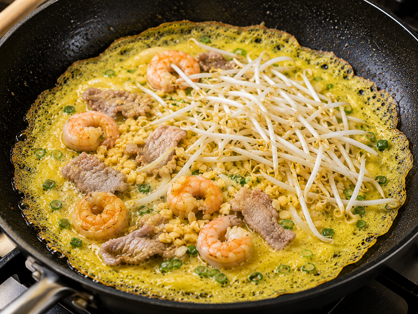 Bean sprouts and cooked mung beans added to a bánh xèo pancake with shrimp and pork in a skillet.
