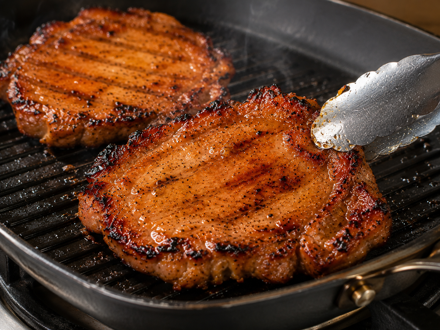 Pork chops for Cơm Tấm sizzling in a grill pan with caramelized edges, char marks, and a glossy fish sauce marinade.
