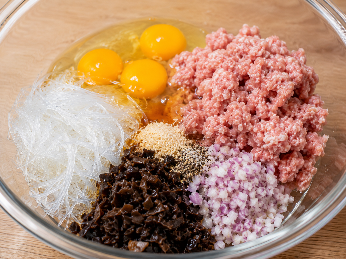 Egg meatloaf ingredients for Cơm Tấm arranged in a mixing bowl with ground pork, eggs, glass noodles, wood ear mushrooms, shallot, fish sauce, salt, sugar, and black pepper.