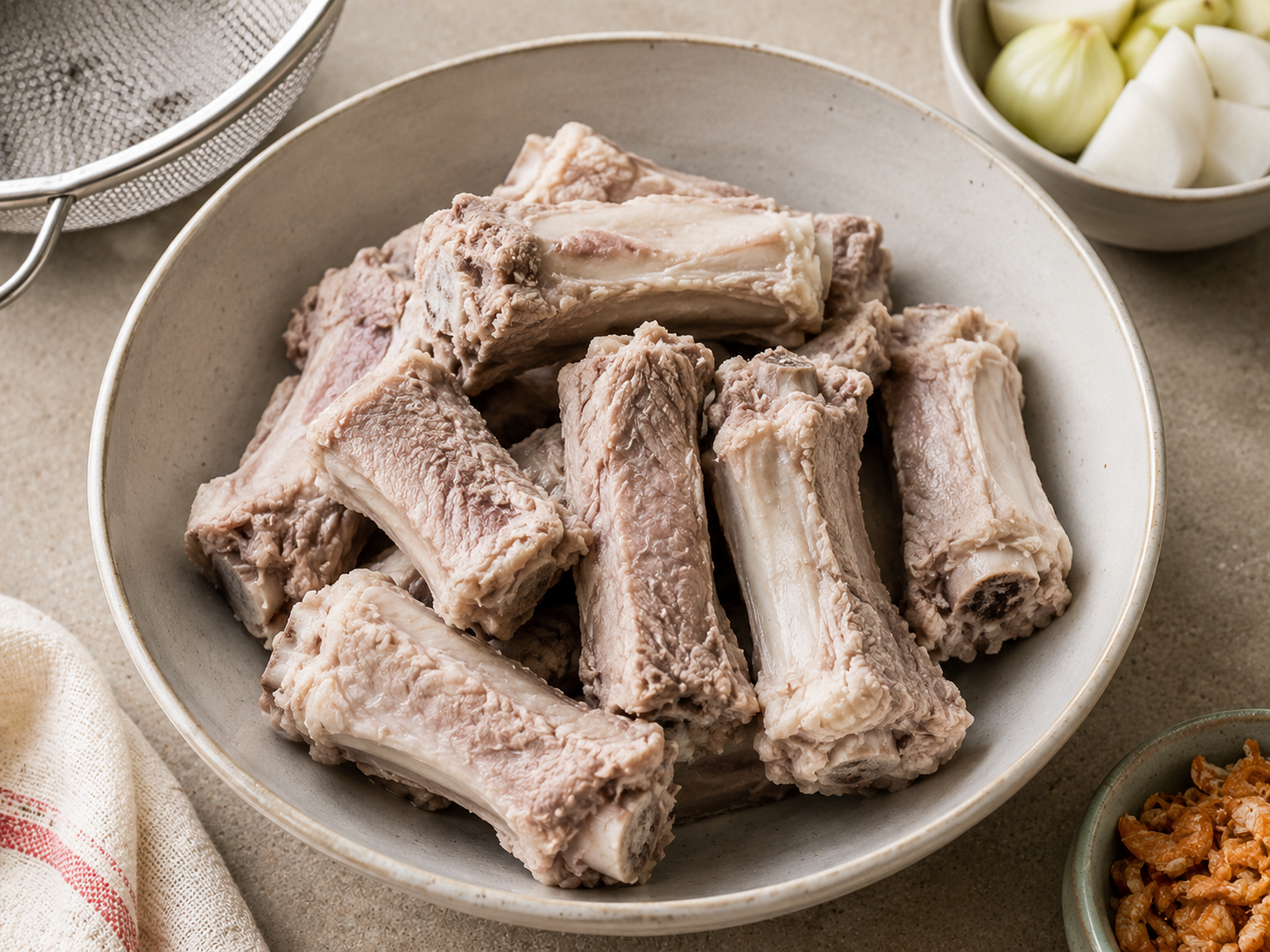 Cleaned pork bones for bánh canh cua broth after blanching and rinsing, with onion, daikon, and dried shrimp nearby.