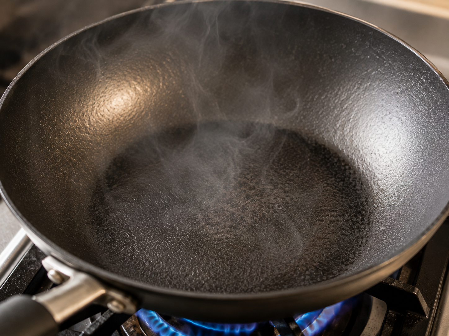 A wok heating over a high gas flame until faint wisps of smoke appear before searing the beef for bò lúc lắc.