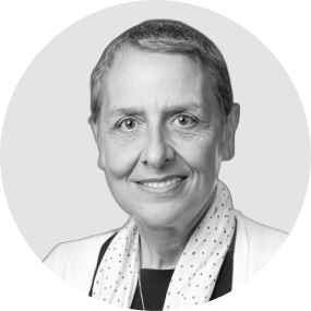 Black and white portrait of a smiling woman with short hair, wearing a light-colored blazer and scarf.