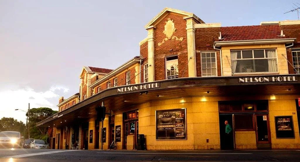 The Nelson Hotel building with a curved yellow facade, large windows, and a mix of brick and cream exterior, at sunset.