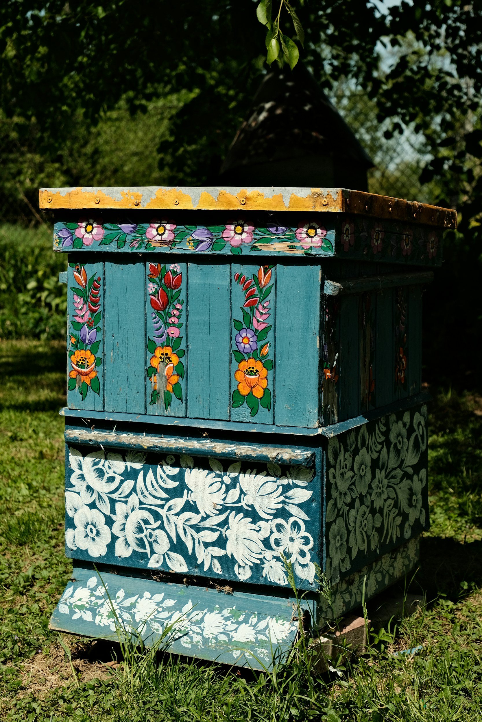 Colorful painted wooden boxes stacked outdoors in a grassy area, decorated with floral and leafy patterns.