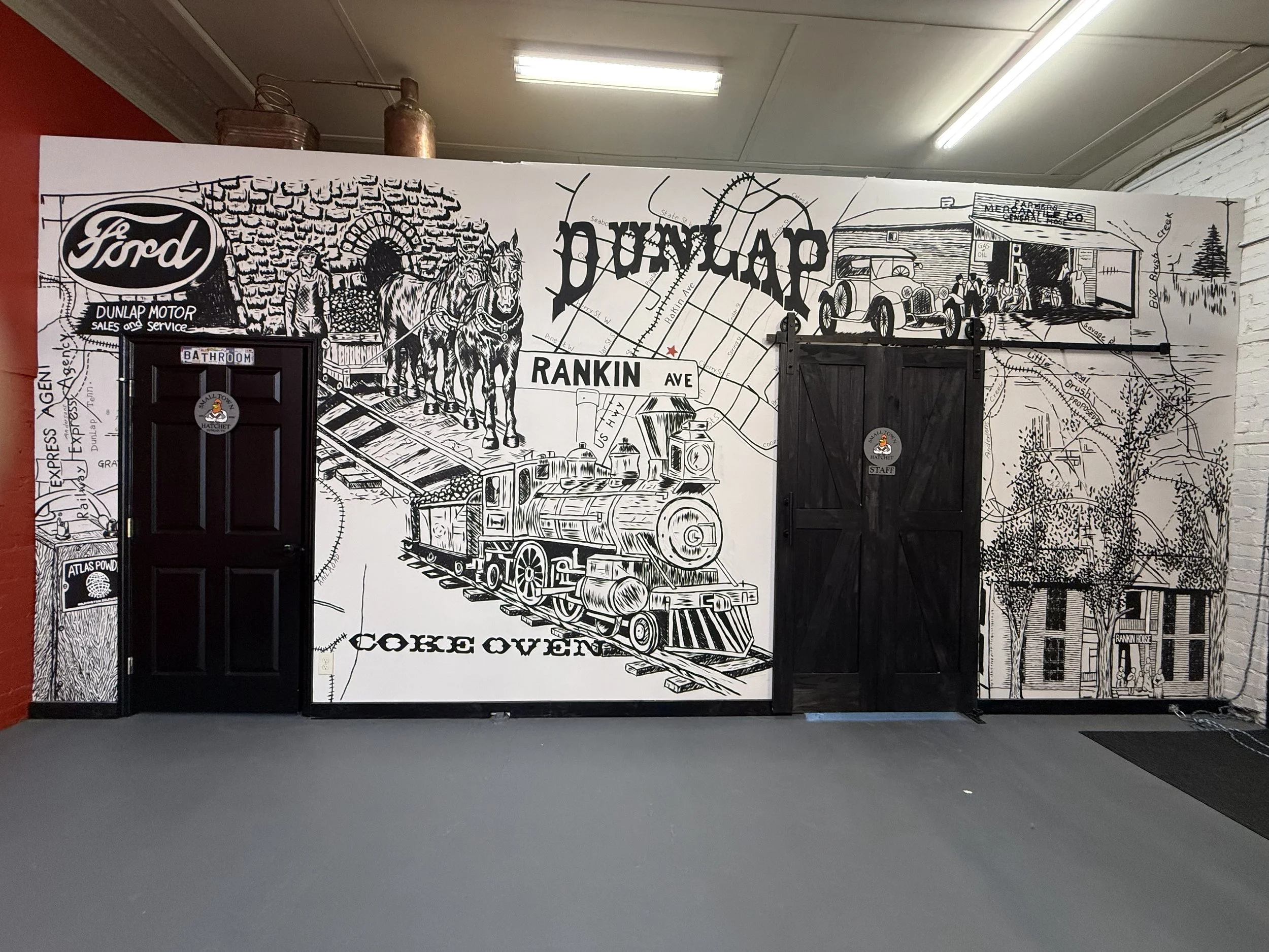 Black and white mural of a vintage train, horses pulling a wagon, historical buildings, and a map with street names, on a wall inside a building.