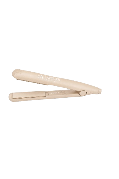 A beige hair straightener with the words 'ATELIER' and 'A' logo on it, open and resting on a glass surface.
