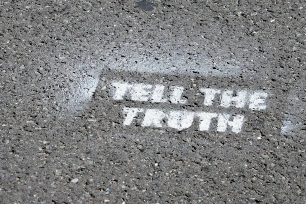 A chalk message on the pavement that reads 'TELL THE TRUTH'.