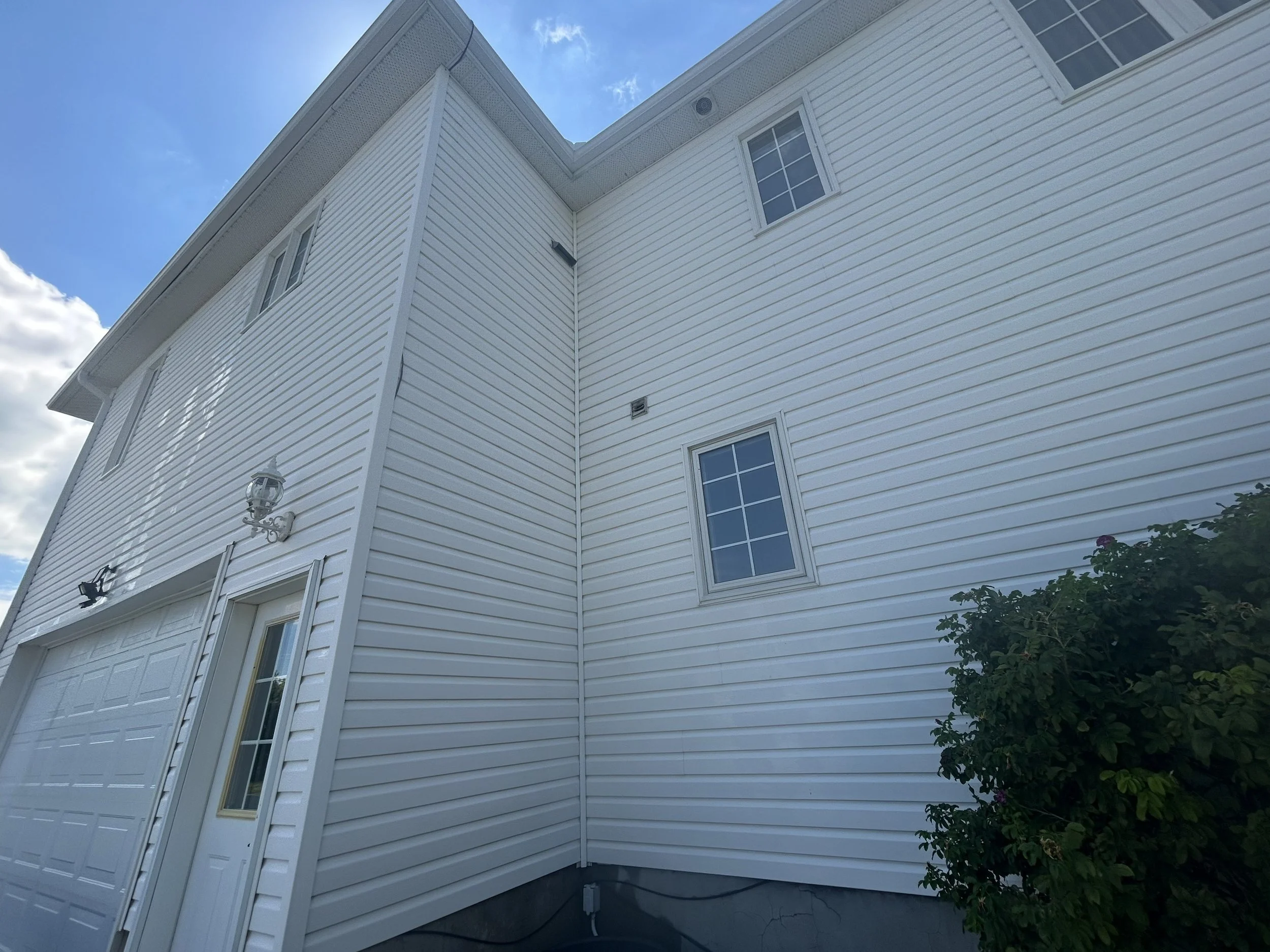 Close-up of the white exterior siding of a house with windows and a garage door, under a blue sky with clouds.