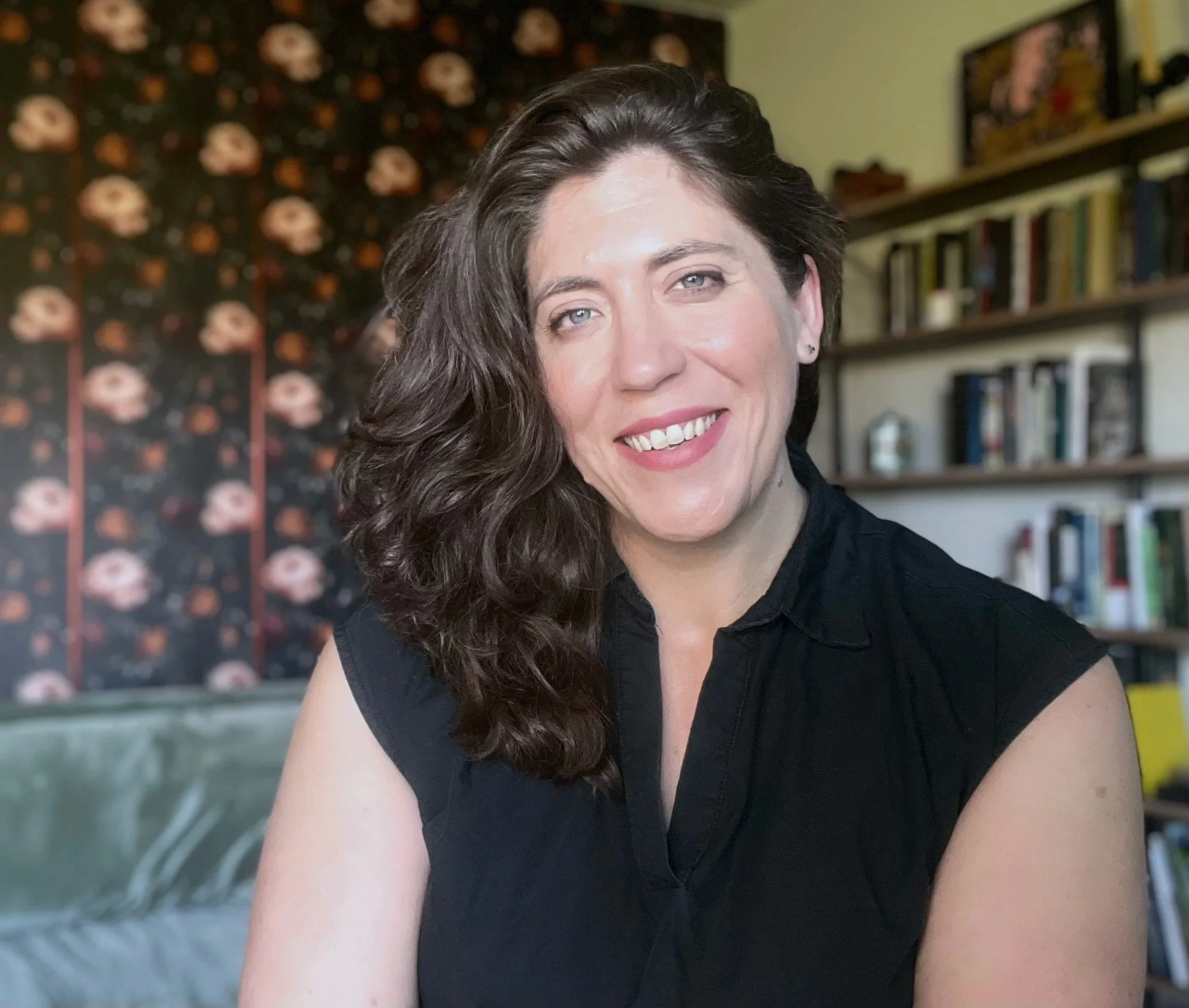 Jennifer Vulgan smiling while seated in therapy office, with bookshelves and artwork in the background.