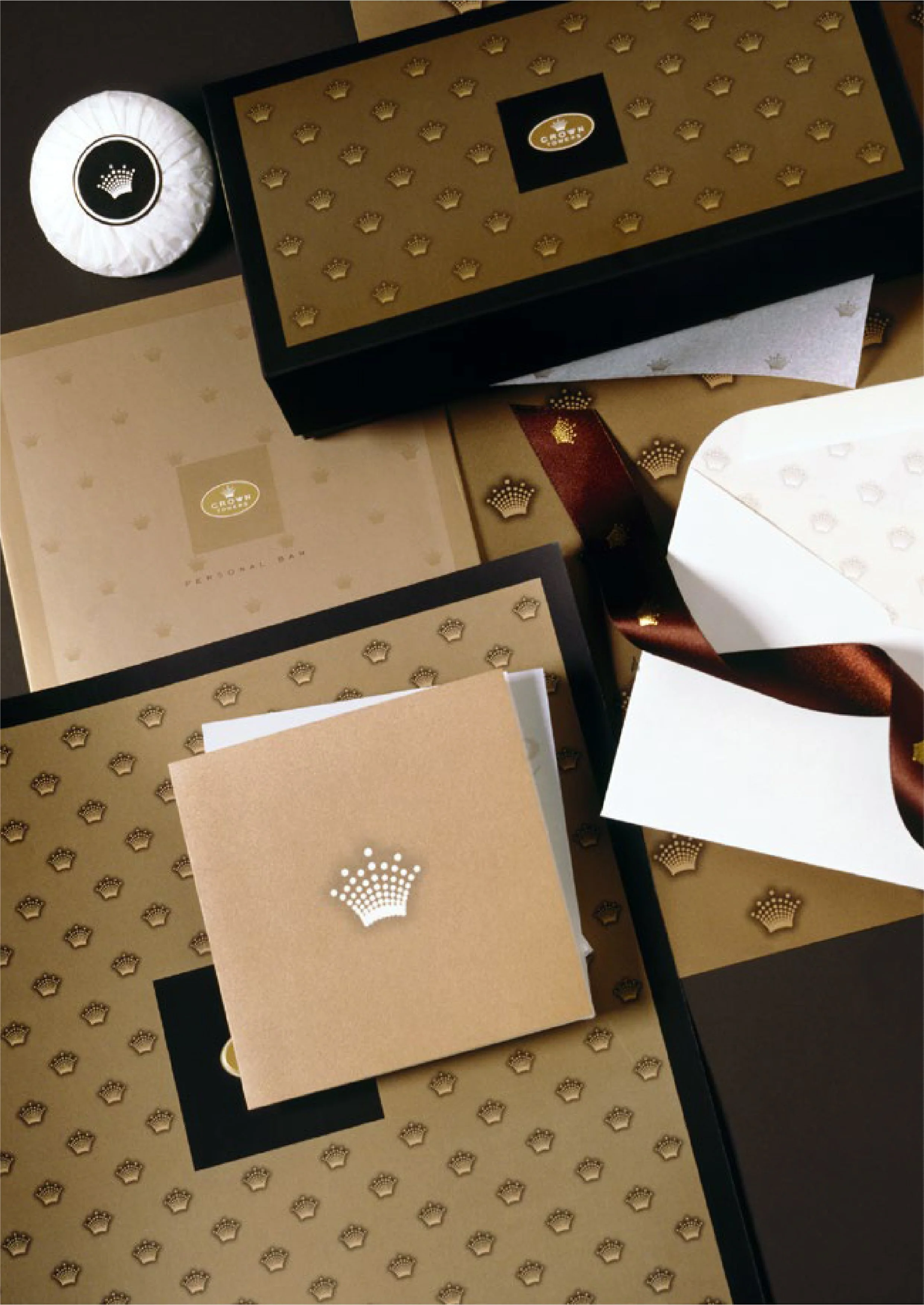 Assorted gift boxes with gold, white, and black packaging, featuring crown logos and decorative patterns. Some boxes are open with tissue paper inside.