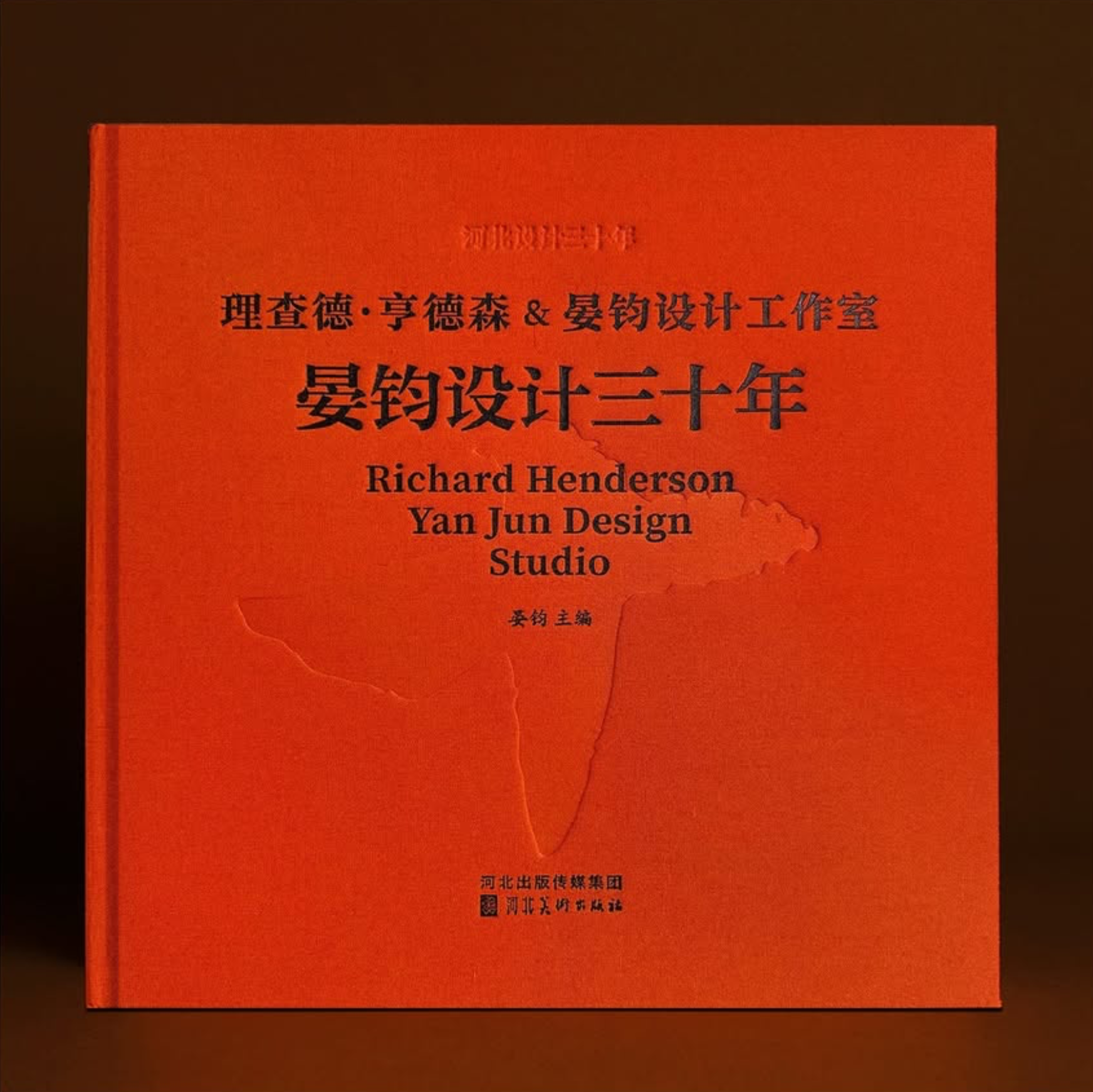 A red book with Chinese characters and English text on the cover, titled 'Richard Henderson Yan Jun Design Studio,' with a faint outline of a map or shape on the cover.