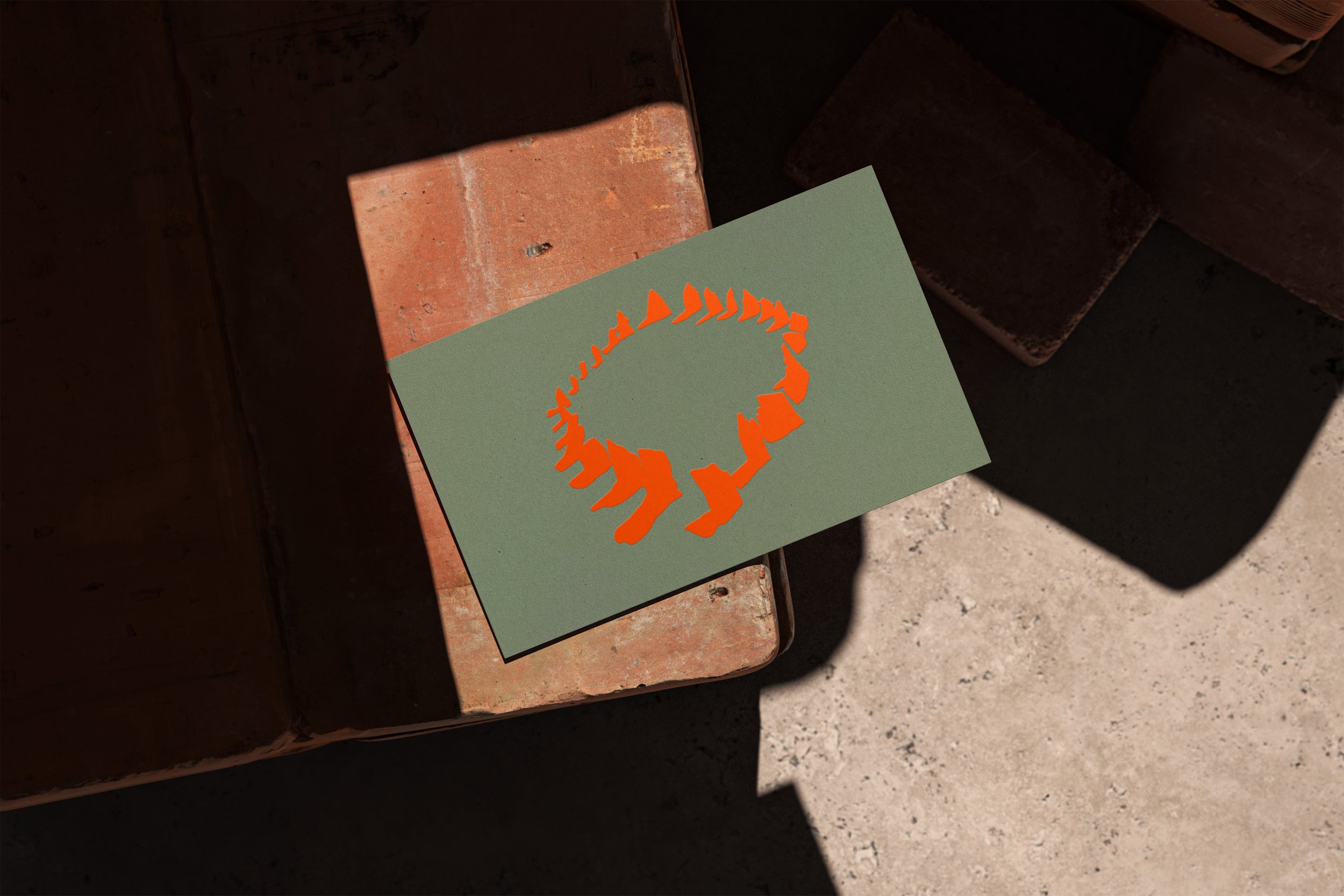 A green card with an orange dinosaur footprint is resting on a rusty brick surface, with shadows cast across the scene.