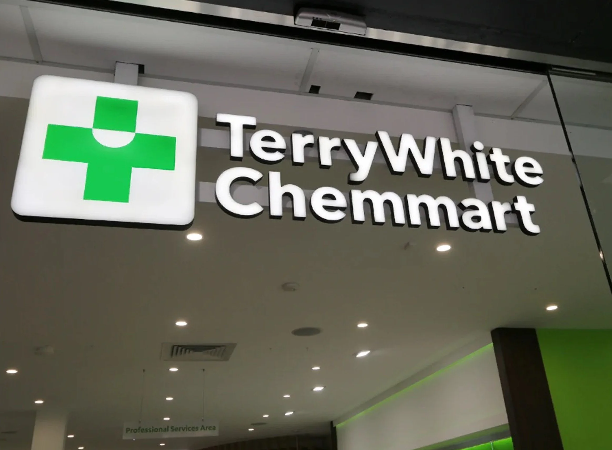 Retail store sign for 'TerryWhite Chemmart' with a green pharmacy cross logo, displayed indoors with ceiling lights and a partial view of the store interior.