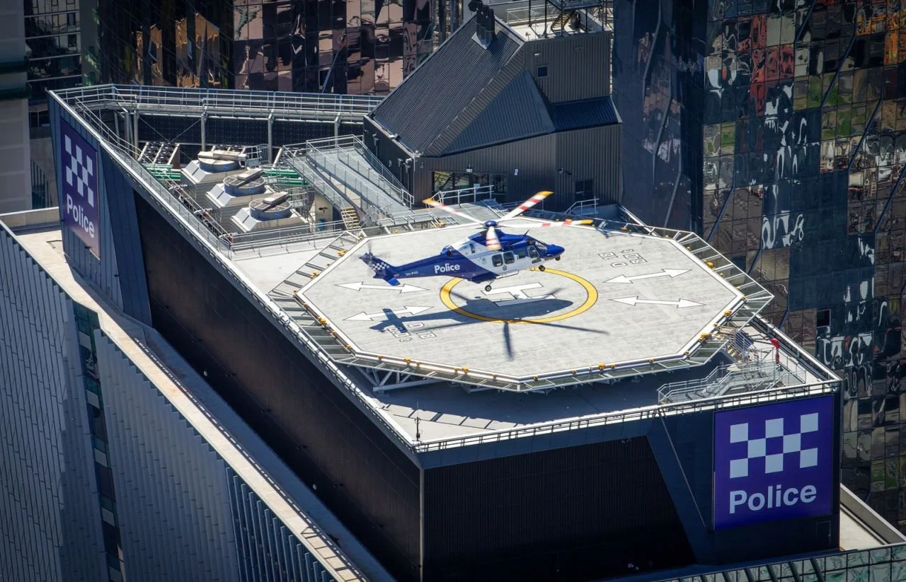 A police helicopter parked on a helipad atop a tall building in an urban area, with reflective glass windows and police signs on the building.