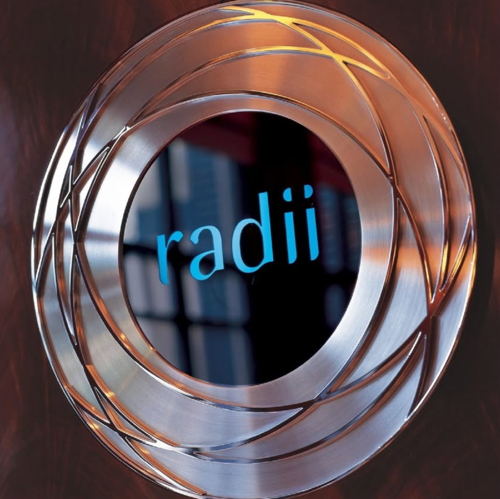 A close-up of a metallic, spiral-shaped object with the word 'radii' through the center, resting on a dark wooden surface.
