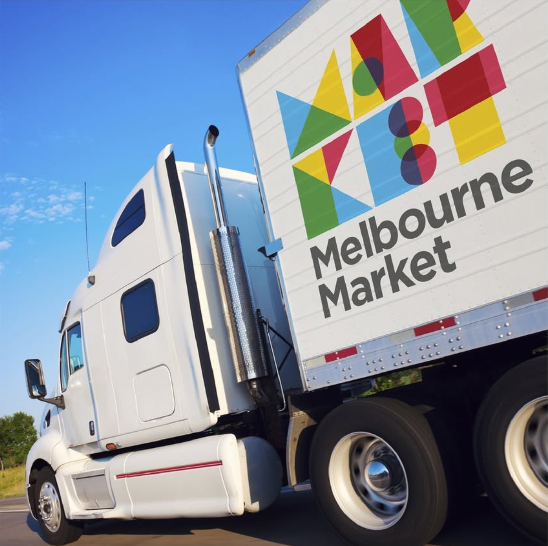 White semi-truck with colorful sign for Melbourne Market on the side, driving on a road under a clear blue sky.