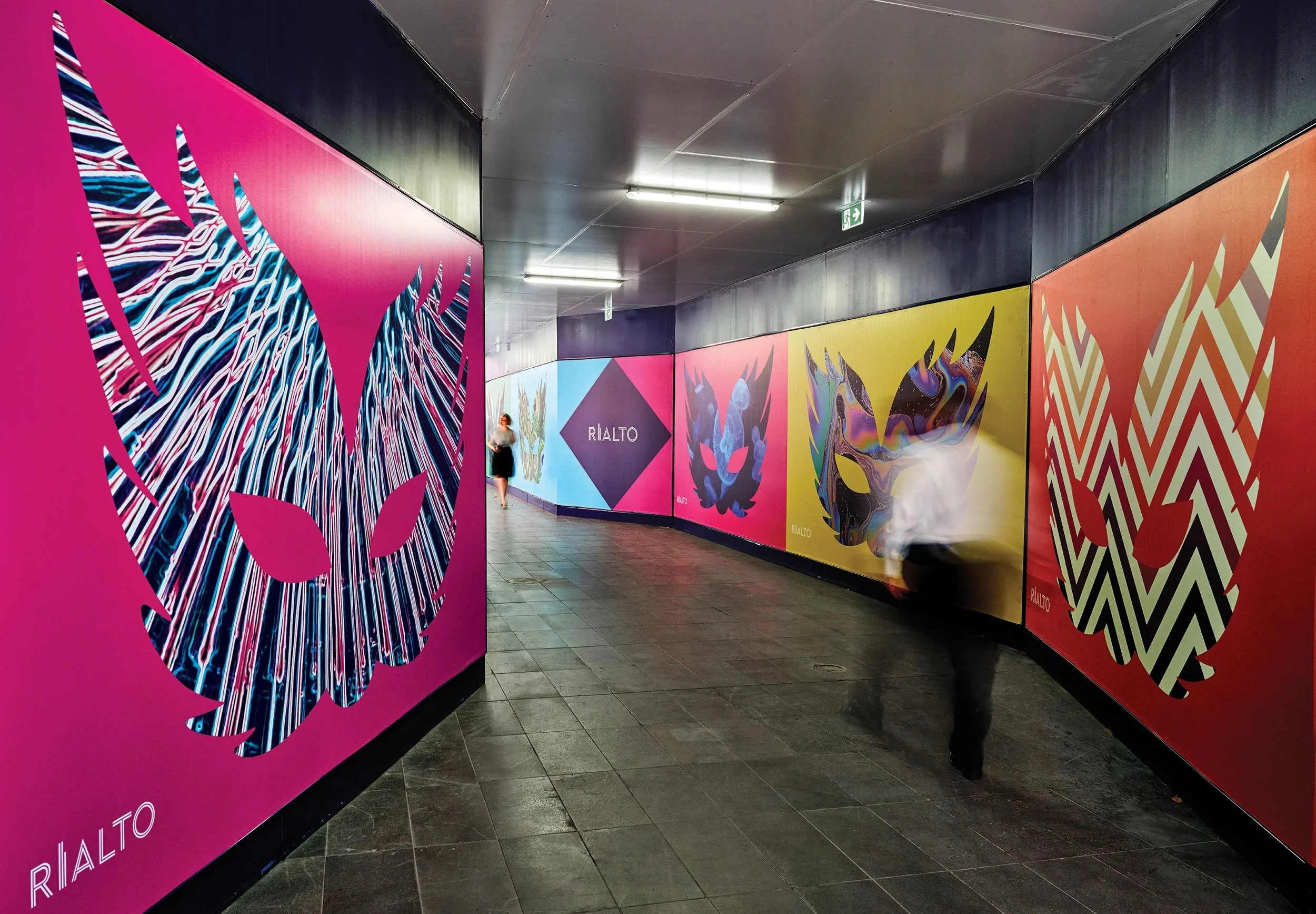 Colorful art installation in an underground passage with large panels displaying abstract designs and a sign reading 'RIALTO' on one of the panels.