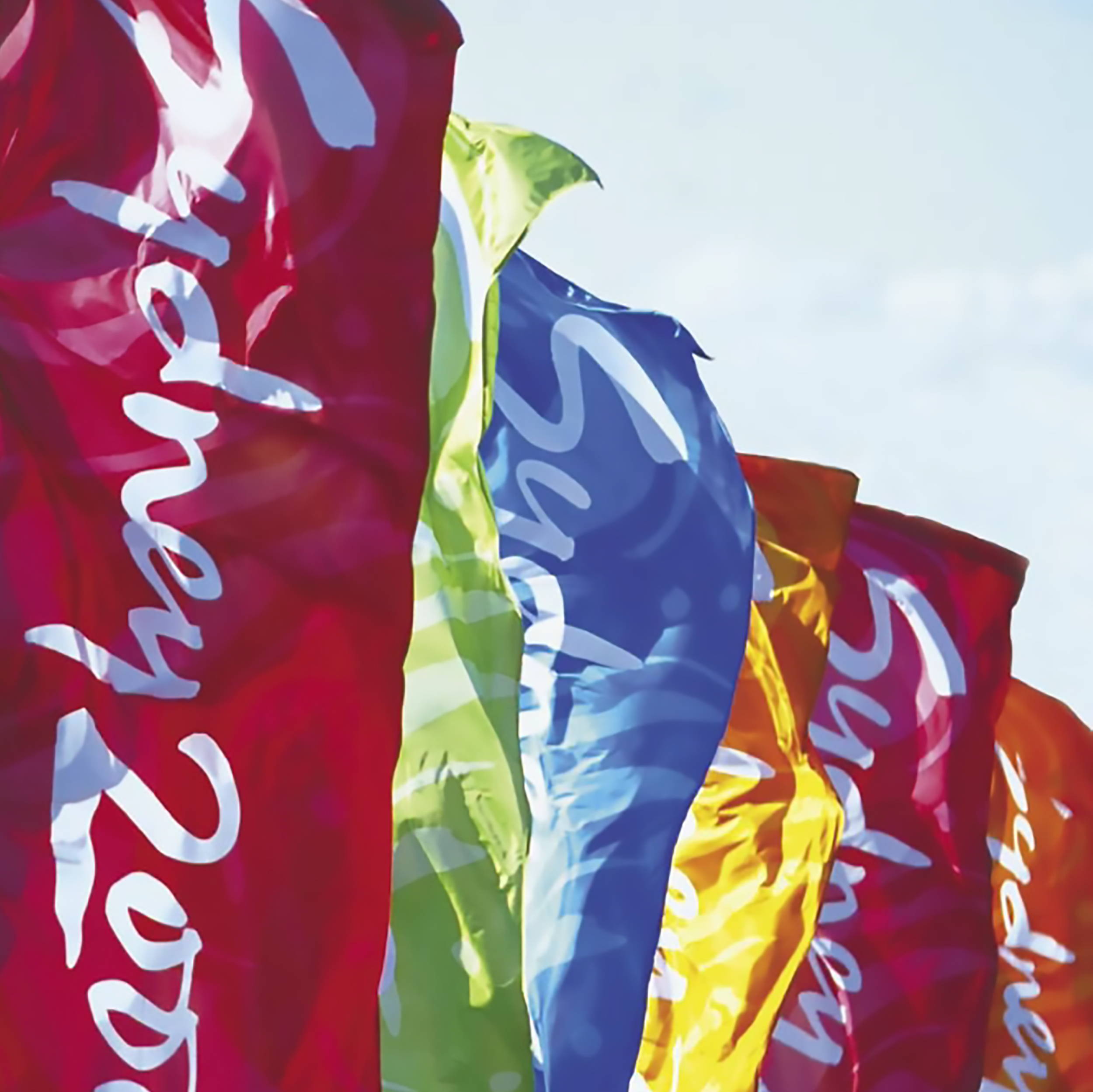 Close-up image of colorful, crinkled paper flags with some text on them, fluttering against a light sky background.