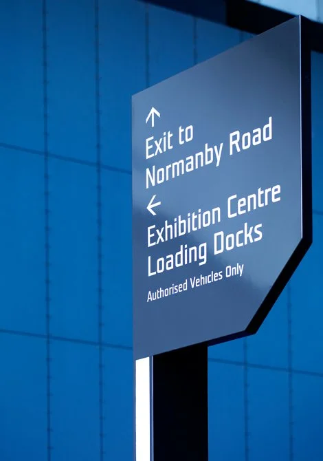 Signpost showing directions to exit, exhibition center, loading docks, and an authorized vehicles only area.