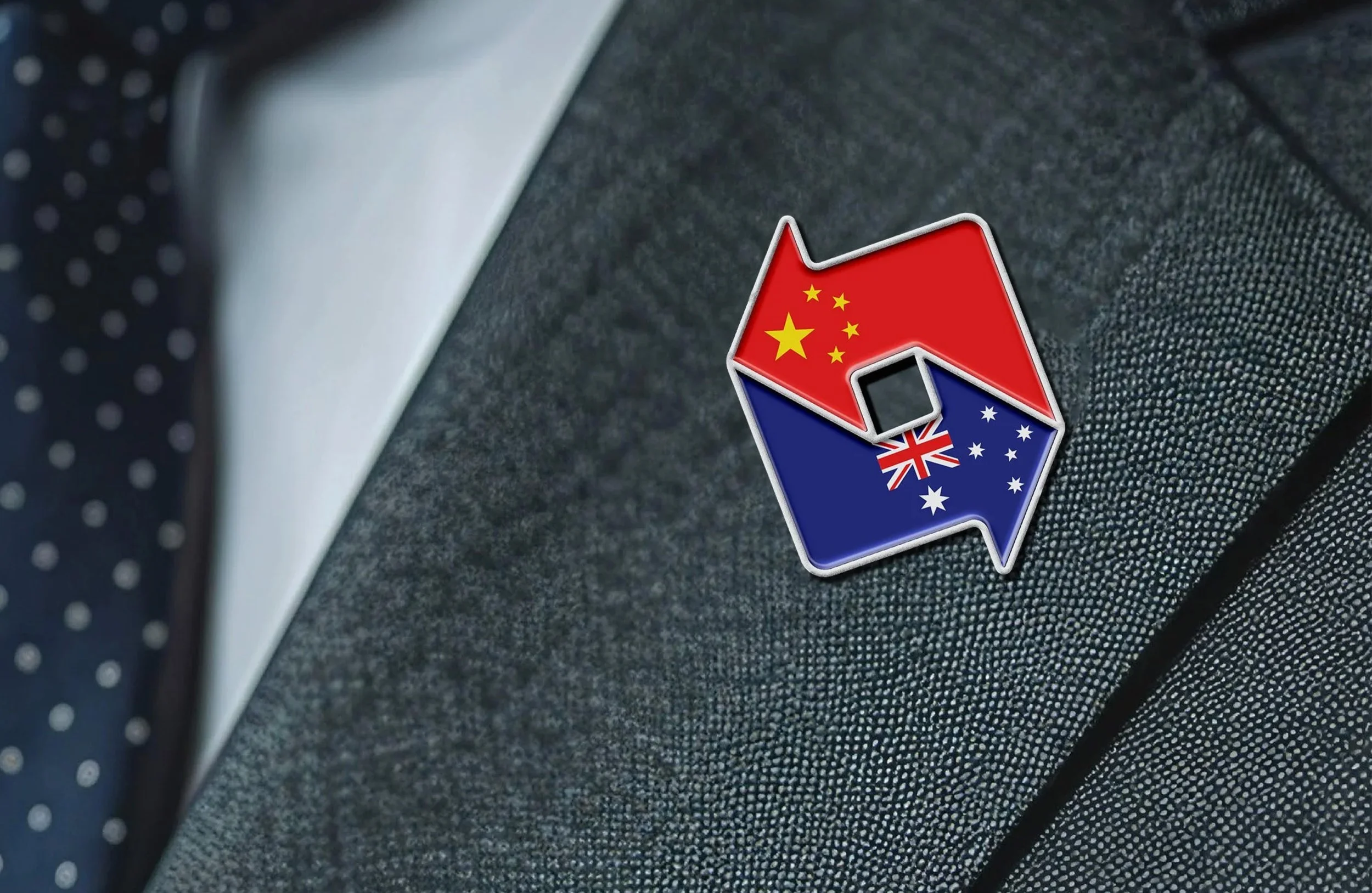 A pin badge featuring the flags of China, the United Kingdom, and Australia, placed on a dark fabric surface.