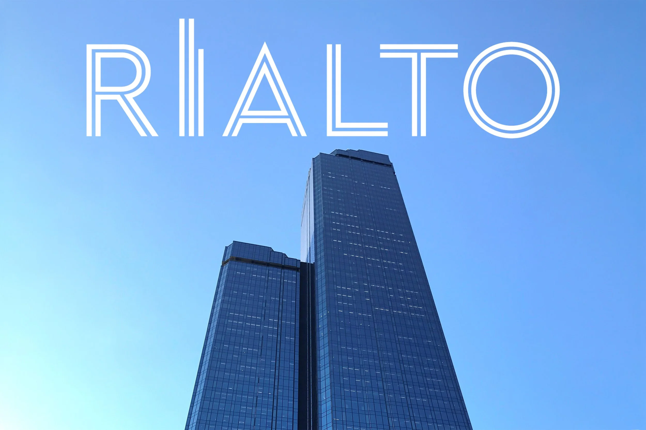 A tall modern skyscraper with reflective glass windows against a clear blue sky, with the word 'RIALTO' written in large white outline letters across the sky above the building.
