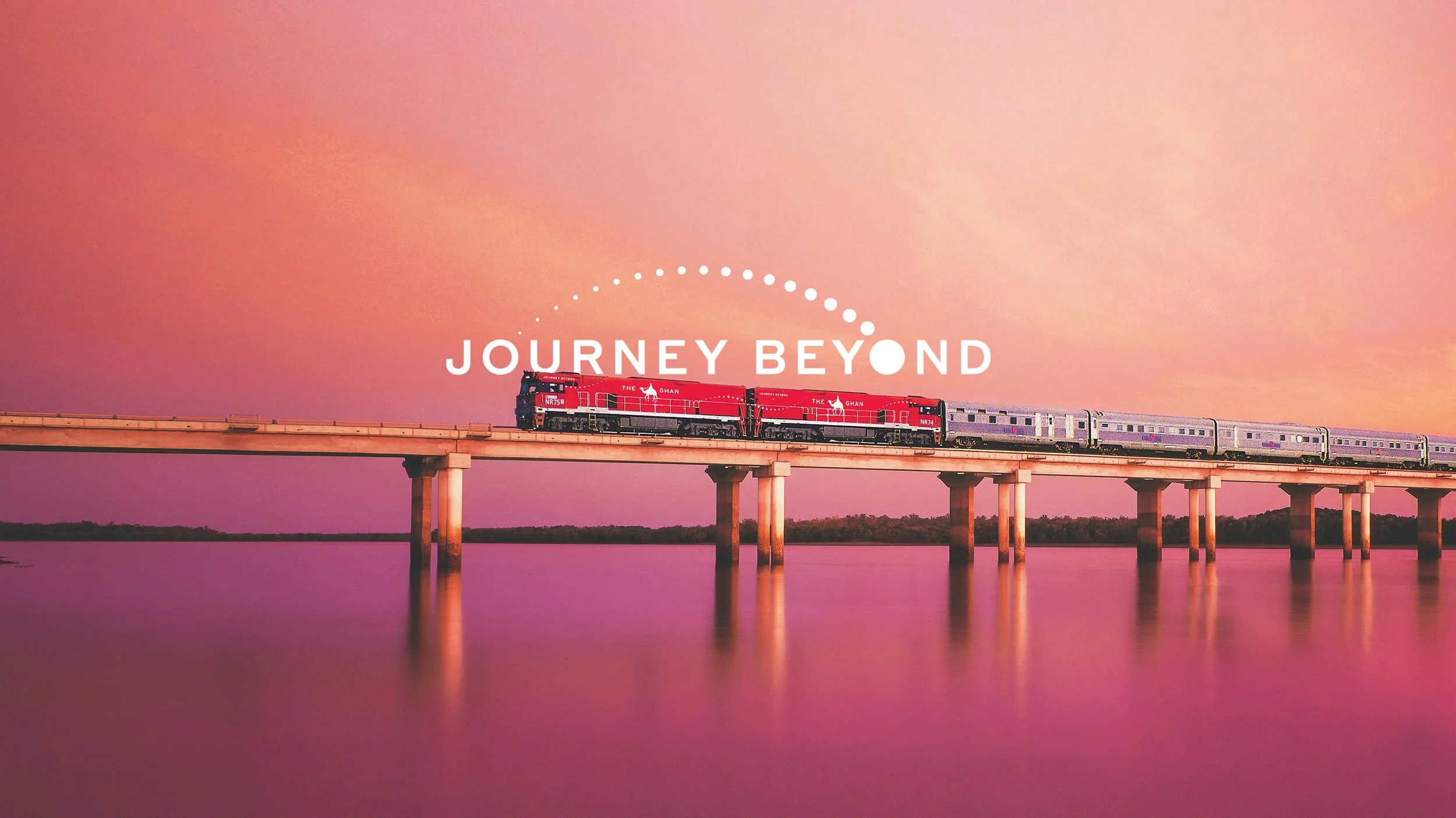 A train traveling on a bridge over a body of water during sunset or sunrise with a pink and orange sky. The words 'Journey Beyond' are overlaid on the image.