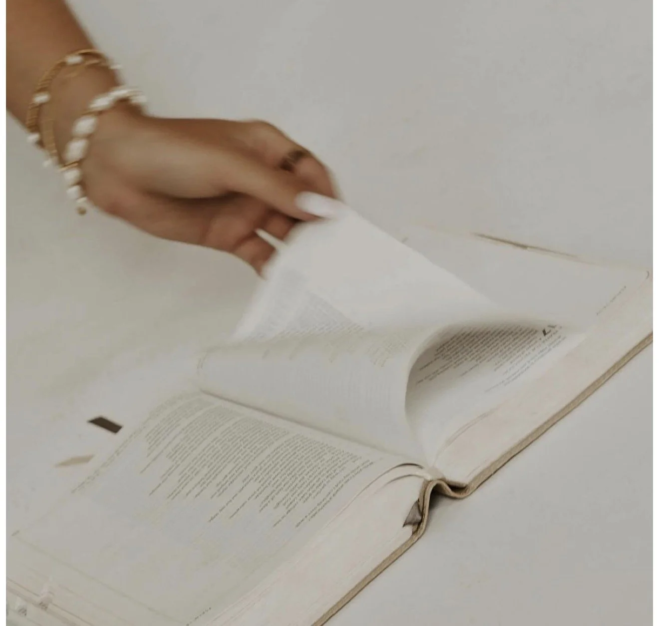 Close-up of a hand turning the page of an open book with a white background.