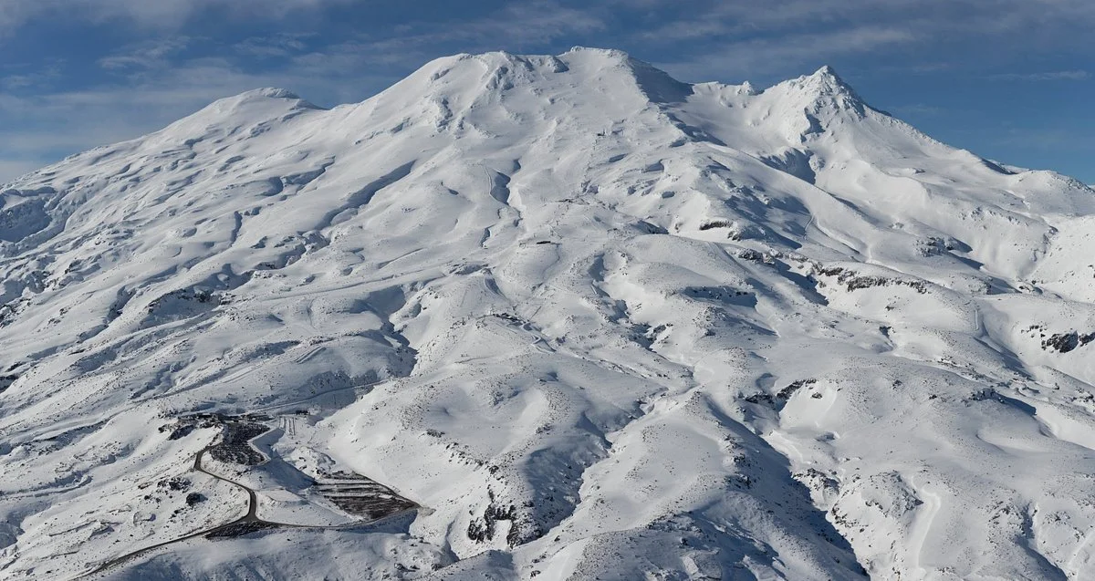 Snow-covered mountain with a ski resort at its base, ski trails visible on the slopes, and a clear sky overhead.