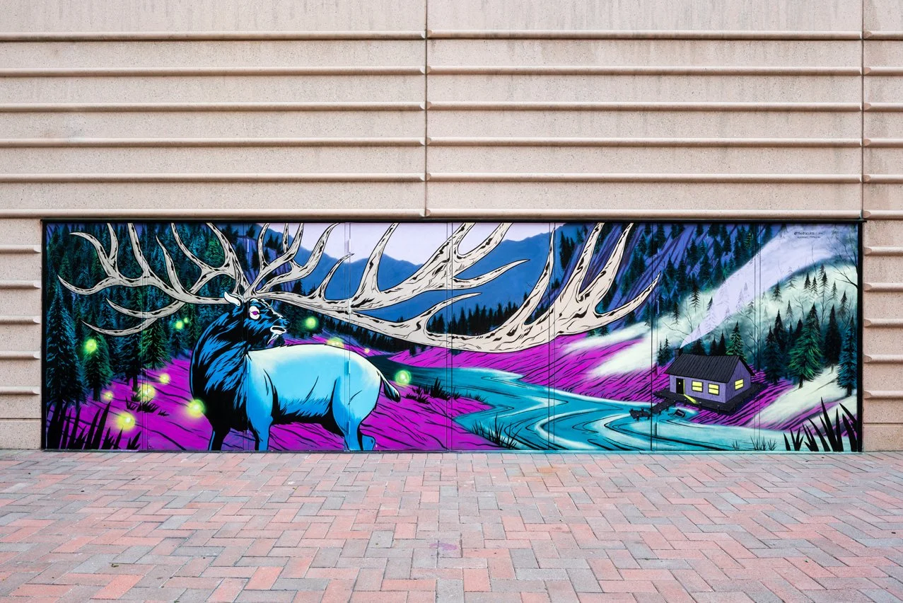 Colorful mural of a moose with large antlers in a forest with purple grass, a winding river, and a small cabin in a mountainous landscape at night.