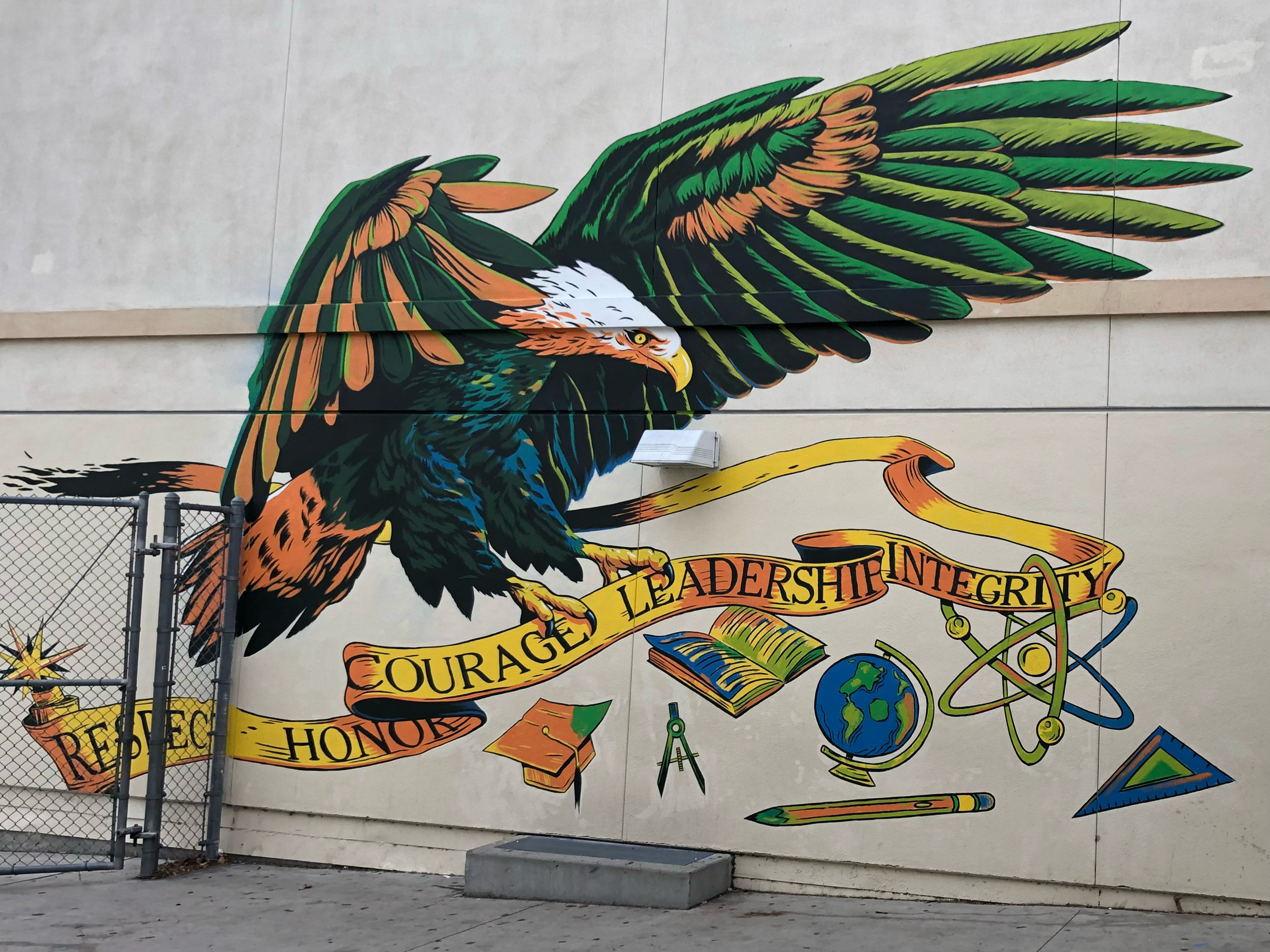A colorful mural of a bird of prey with outstretched wings. The bird's body is detailed with green, orange, blue, and black feathers. Below it, a yellow banner displays words such as "Respect," "Honour," "Courage," and "Leadership". The mural is pain