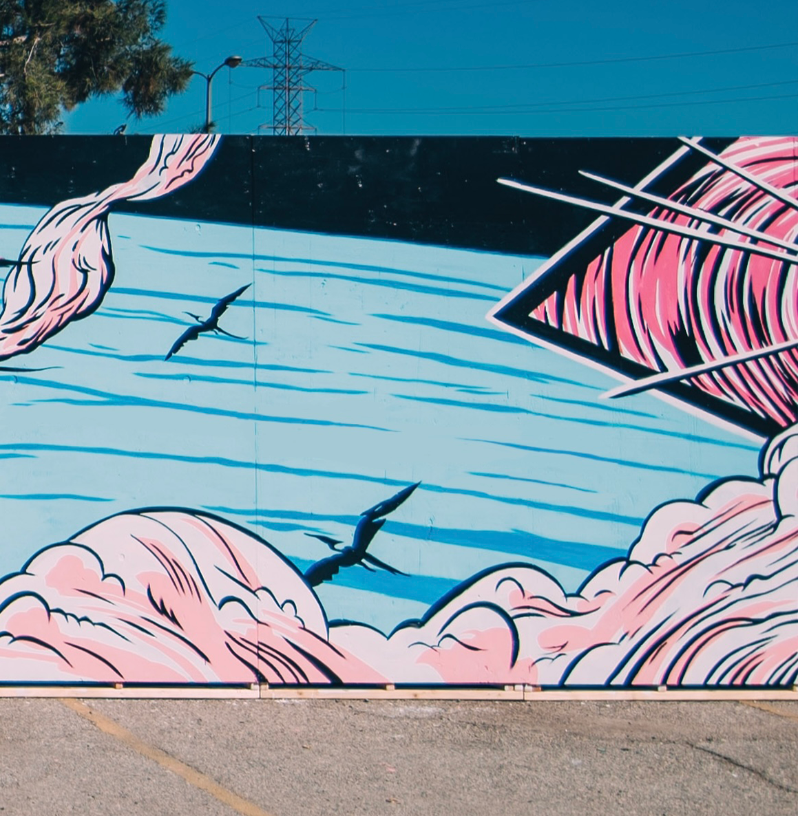 Street art mural featuring pink and black abstract cloud-like shapes, black birds flying over blue wavy lines, and a pink geometric design on the right side.