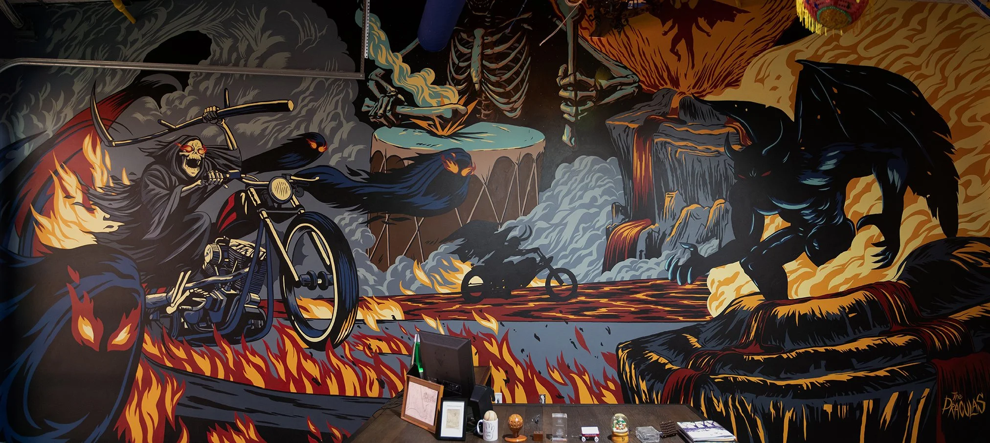 A colorful mural depicting a skeleton with a flaming cloak riding a motorcycle through a fiery landscape with volcanic activity, volcanoes, and demonic creatures.