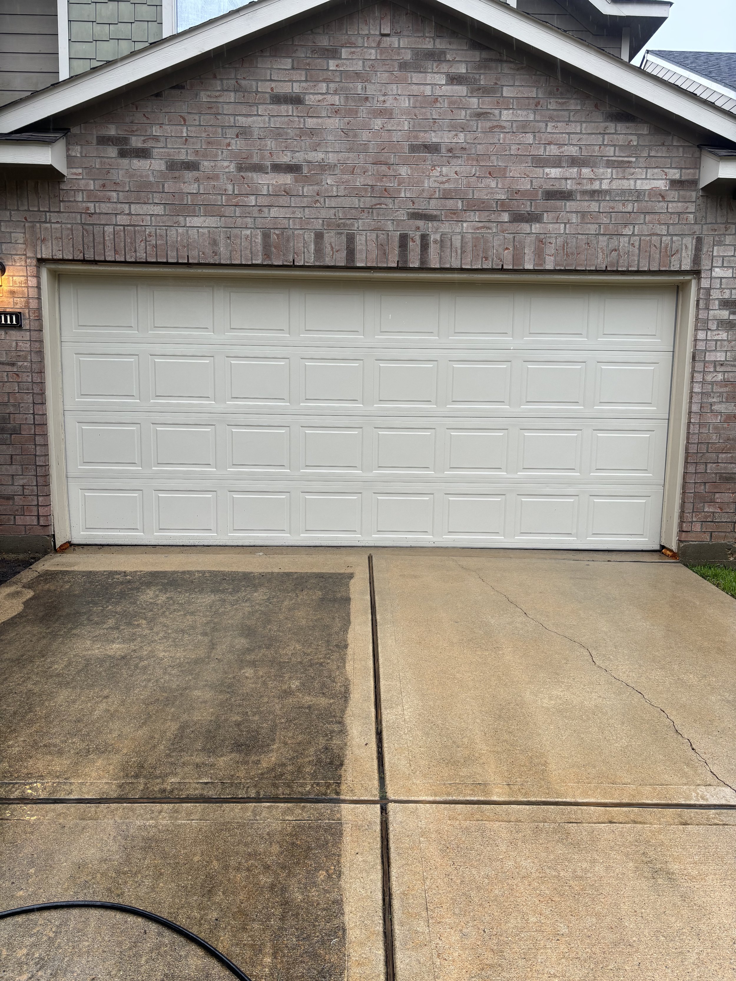 Front view of a garage door with a brick wall and part of a house visible in the background.