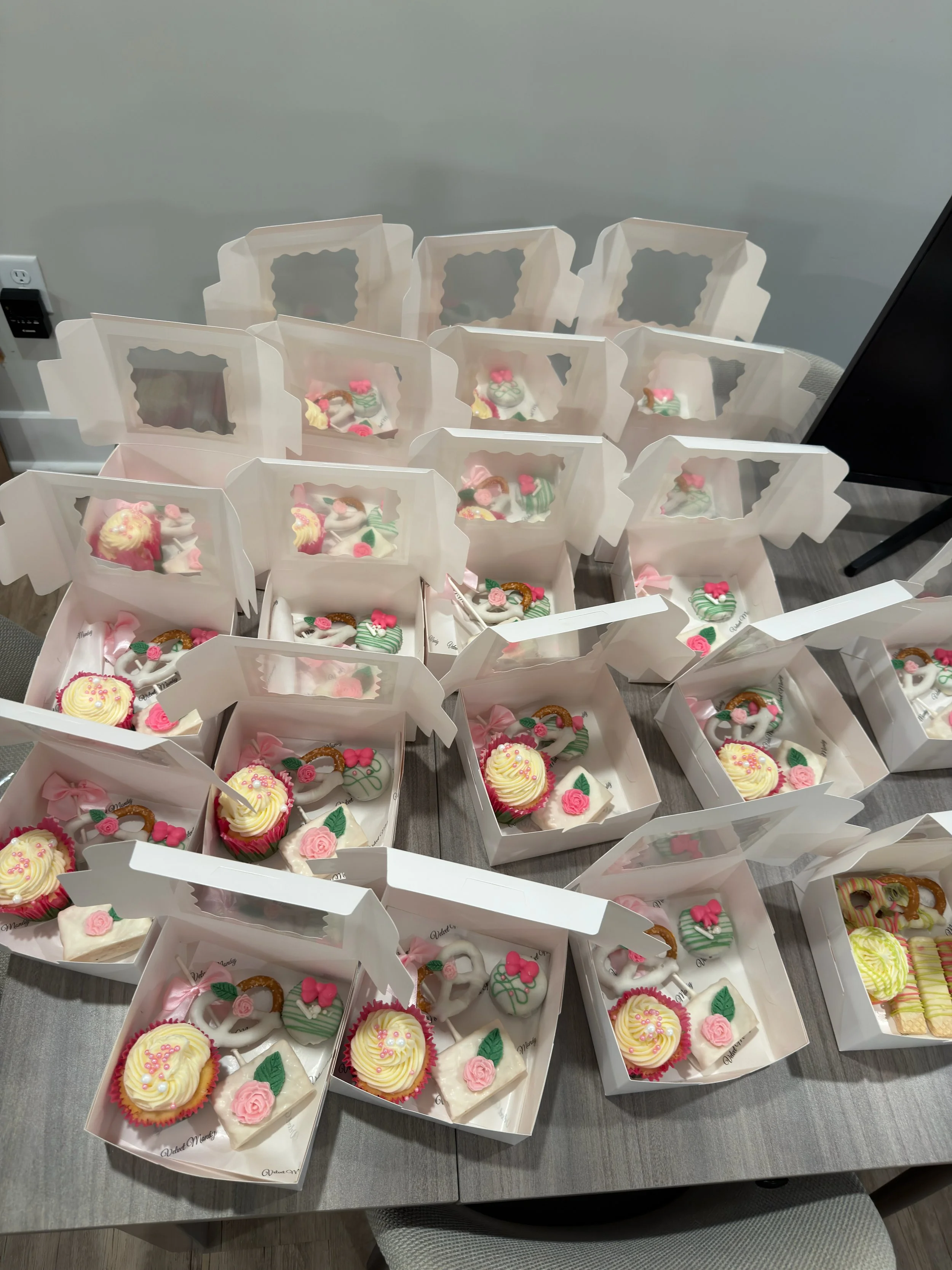 Multiple white boxes with clear windows containing decorated cookies, placed on a gray table.