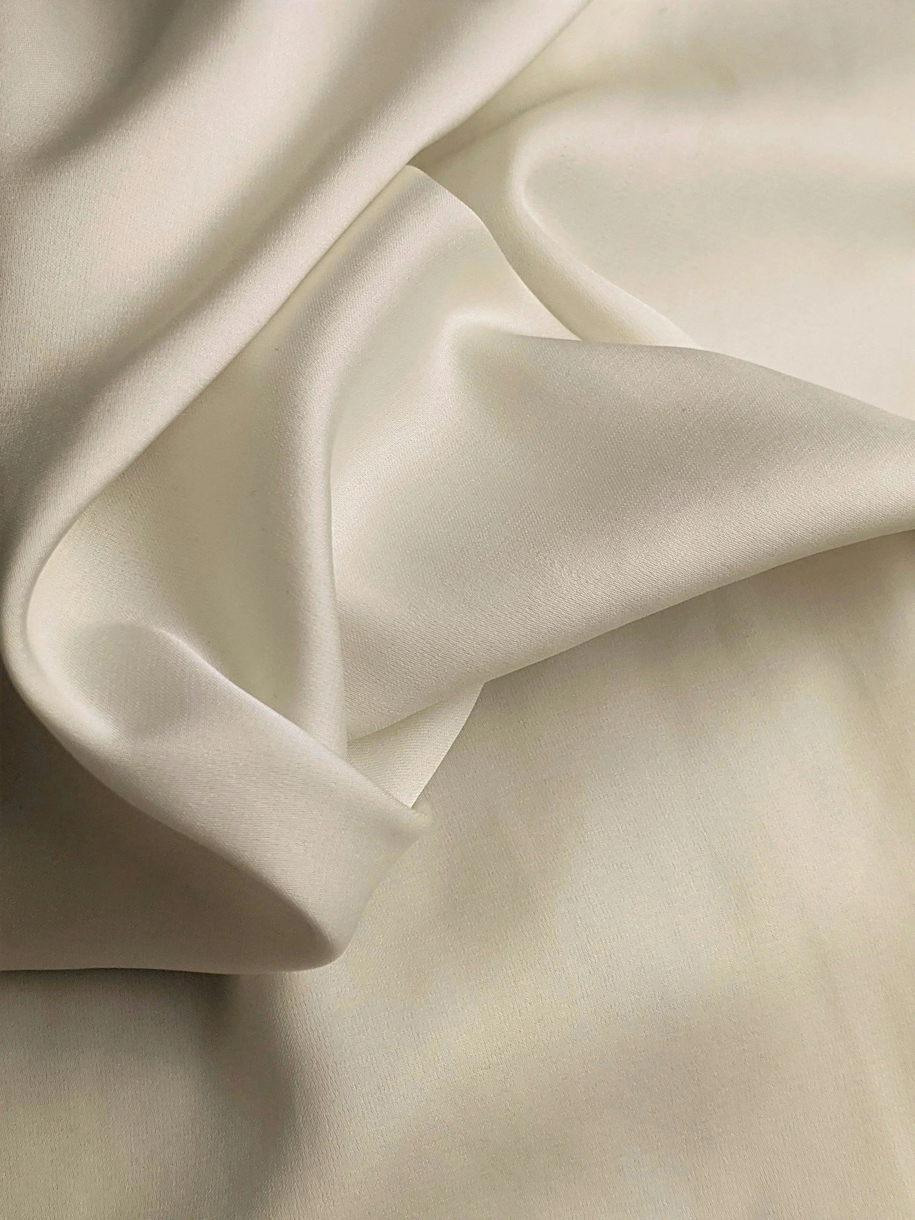 Close-up of ivory silk satin fabric with gentle folds and smooth texture.