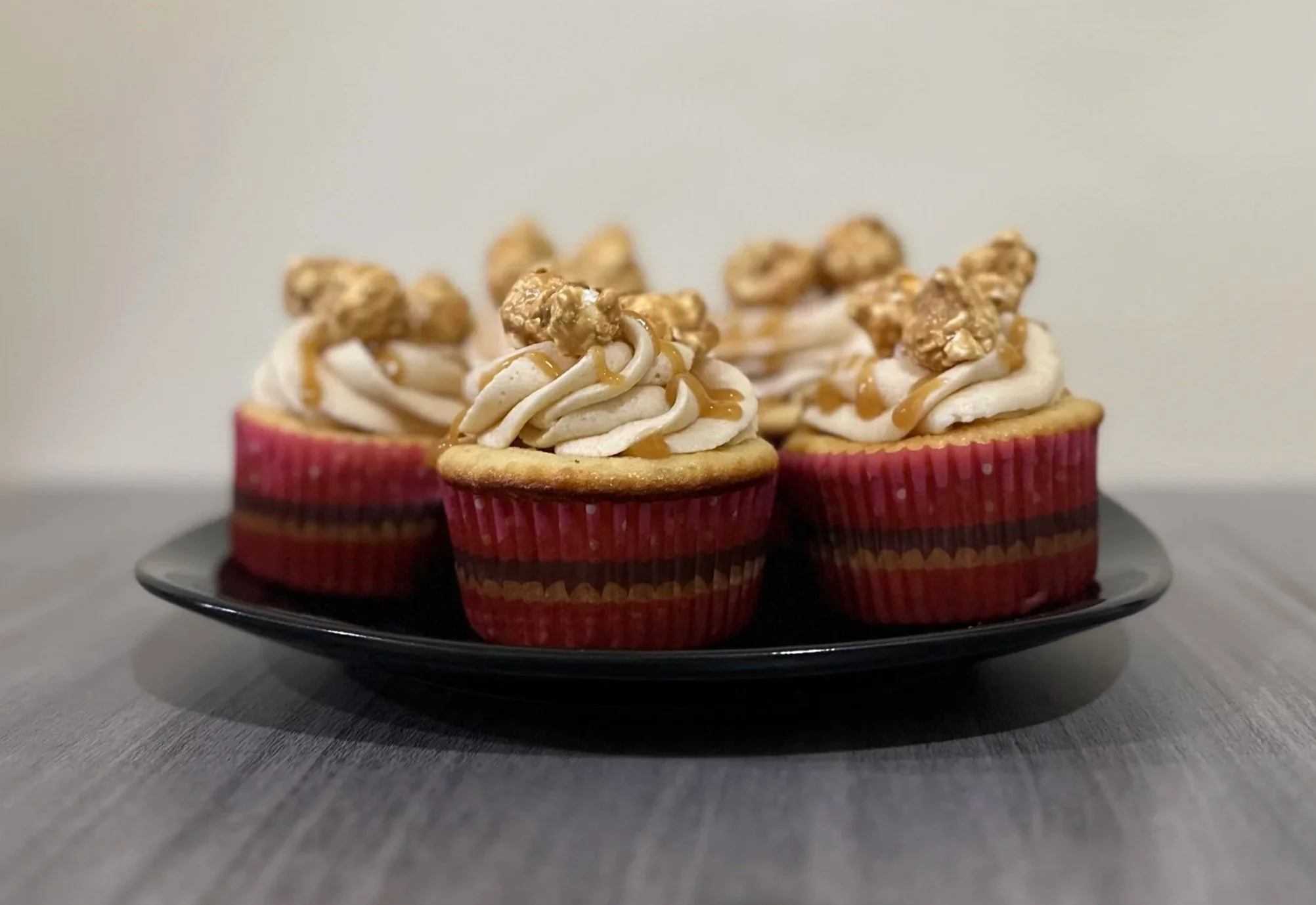 Cupcakes with white frosting, caramel drizzle, and granola topping on a black plate.