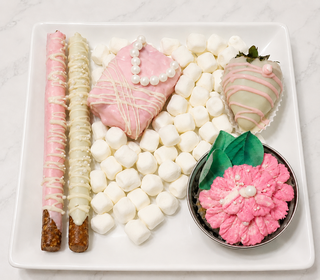 Decorative pink, white, and green confectionery treats and meringue on a white square plate.