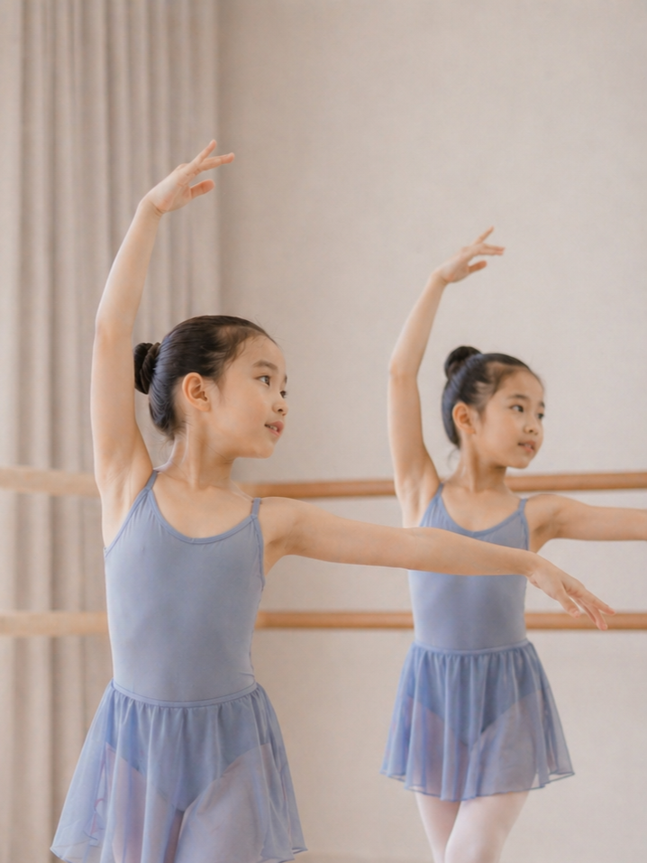 Two young girls in blue ballet tutus practicing ballet in a studio with mirrors.