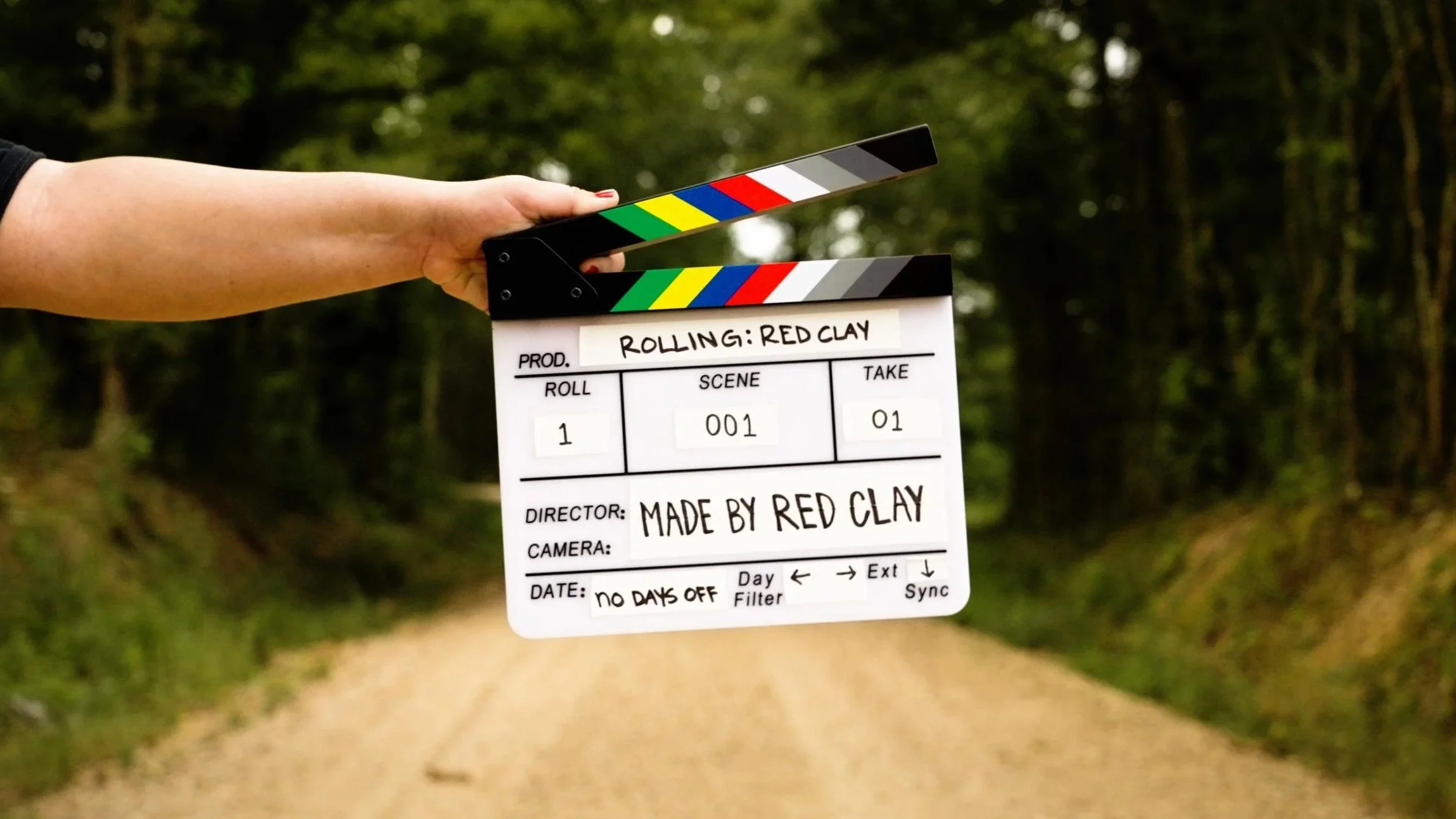 Clapperboard held in a person's hand outdoors with a forest in the background.