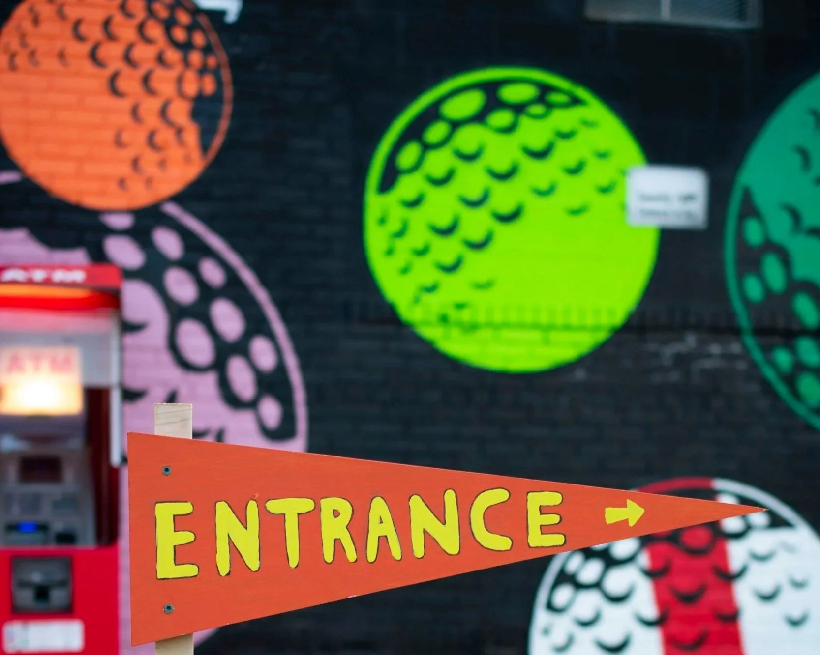 Bright orange sign with yellow letters and an arrow pointing right that says "ENTRANCE" in front of colorful circular patterns on a wall.