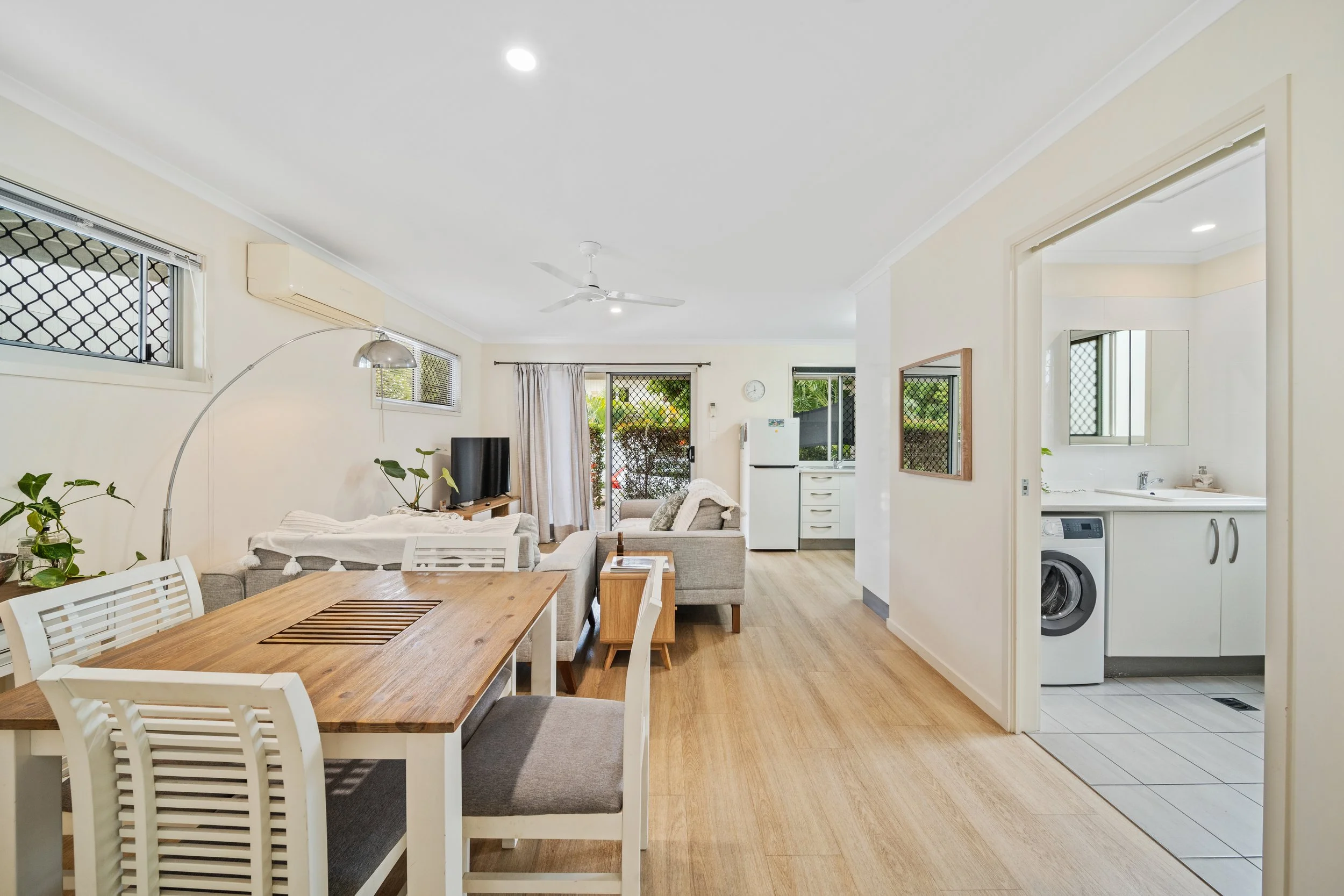 Living room with a dining table, couch, television, and sliding doors leading outside, adjacent to a laundry area in the kitchen.