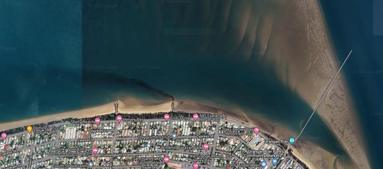 Satellite view of a beachside town with streets, buildings, and a pier leading into the water.