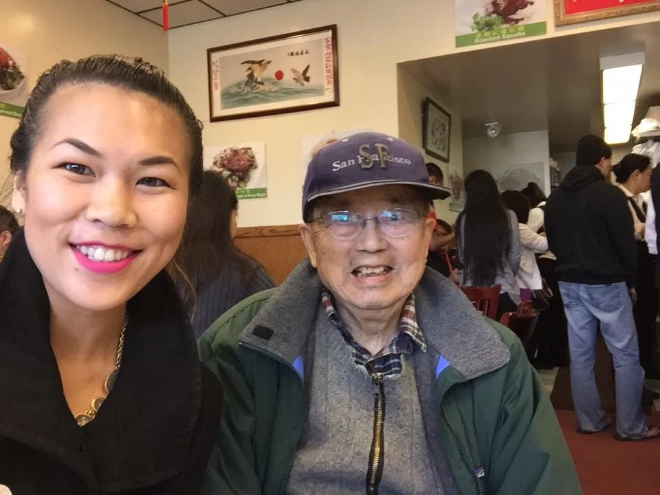 Crystle with her Grandpa smiling at the camera inside a busy restaurant with other diners in the background.