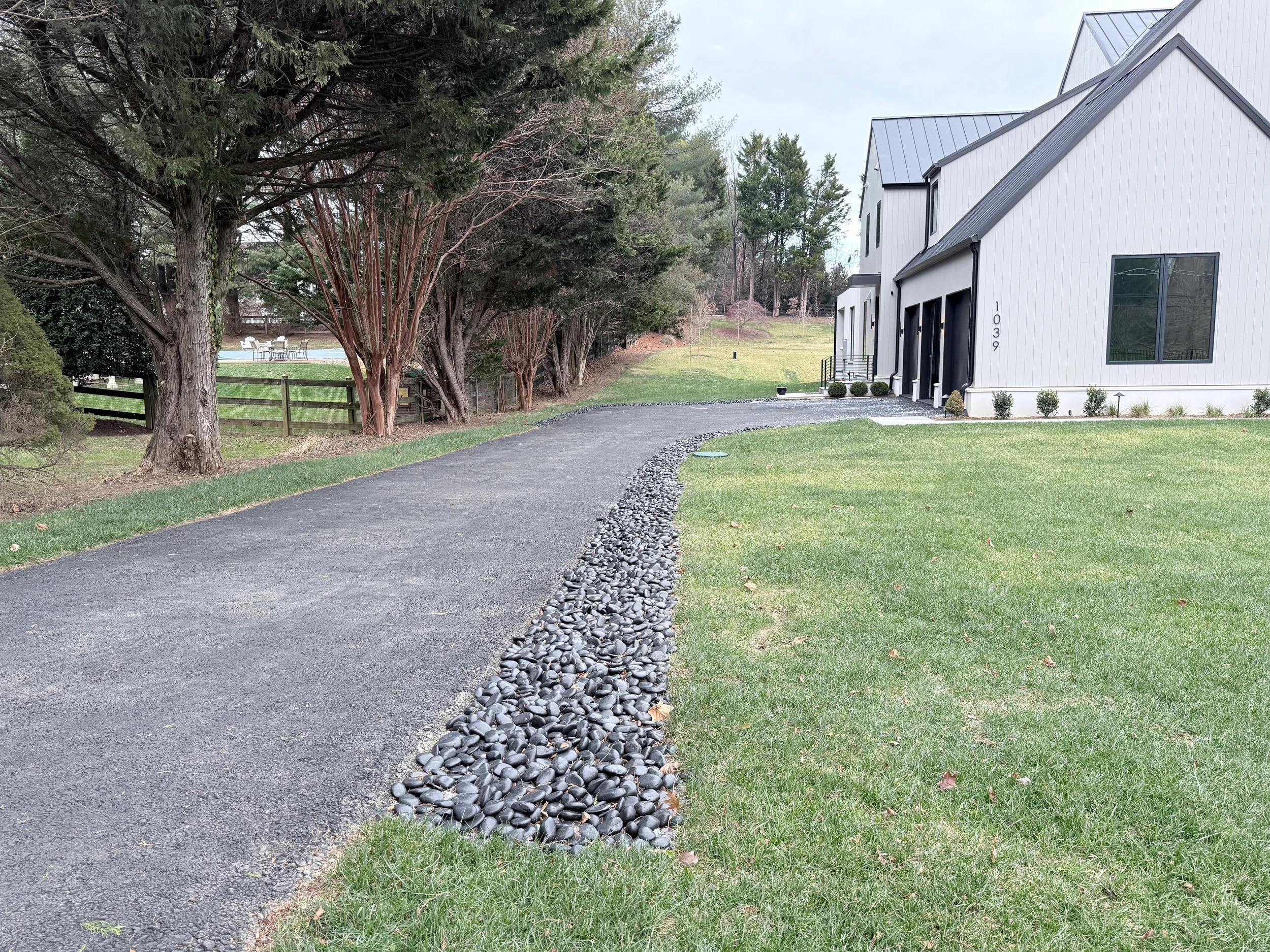 Finished driveway with river rock drainage swale, graded lawn, and clean site restoration for controlled runoff beside a modern home.