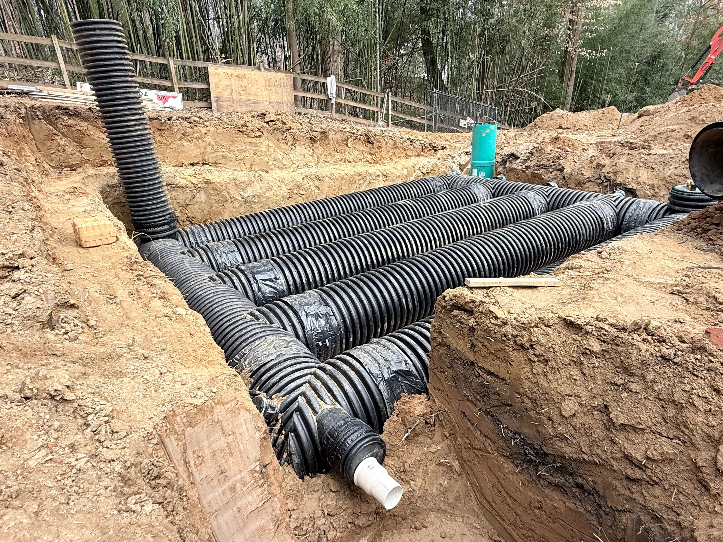 Residential HDPE stormwater detention pipe manifold installed in an excavation with access riser, outlet pipe, and compacted sidewalls.