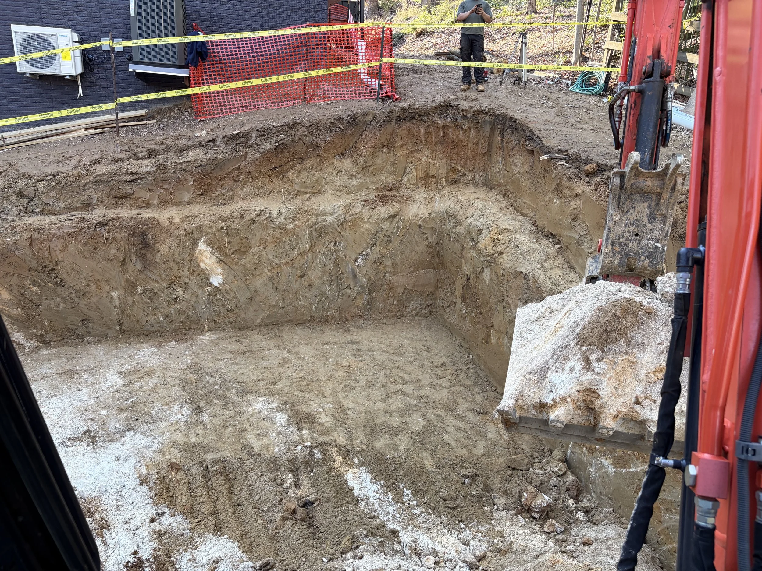 Excavated basin prepared for an underground stormwater detention system, with excavator and safety fencing on a Northern Virginia job site.