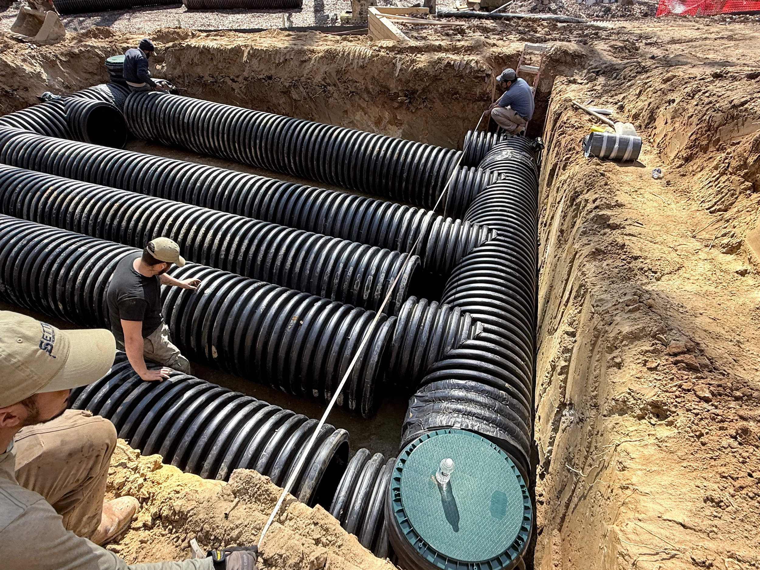 Crew installing corrugated HDPE detention pipes in a deep excavation for an underground stormwater system in Northern Virginia.