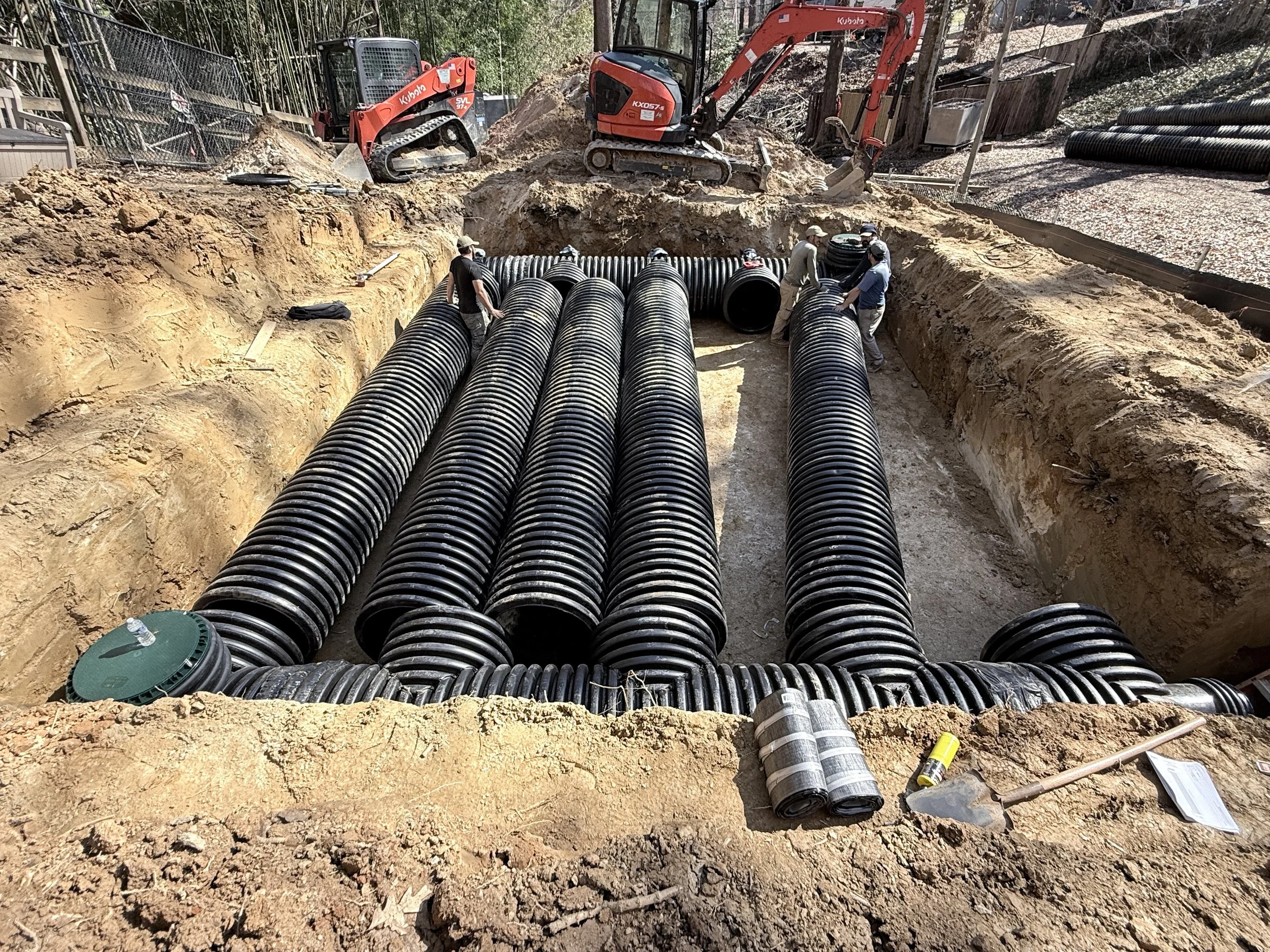 Capital Stormwater Services crew installing rows of corrugated HDPE detention pipe in an open trench using a Kubota excavator in Northern Virginia.